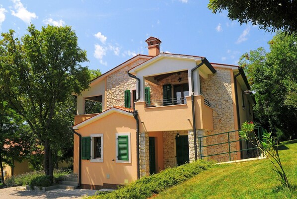 Una casa de dos pisos con fachada de piedra, contraventanas verdes y un balcón.
