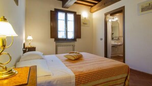 A hotel room with a bed, a nightstand with a lamp, a window with curtains, and a bathroom visible through an open door. - Borgo Fontana by Interhome (Vinci)