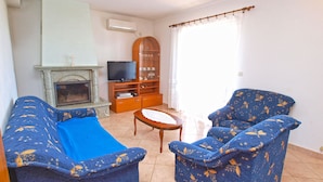 A living room with two blue patterned sofas, a small wooden table, a television on a wooden stand, and a fireplace.