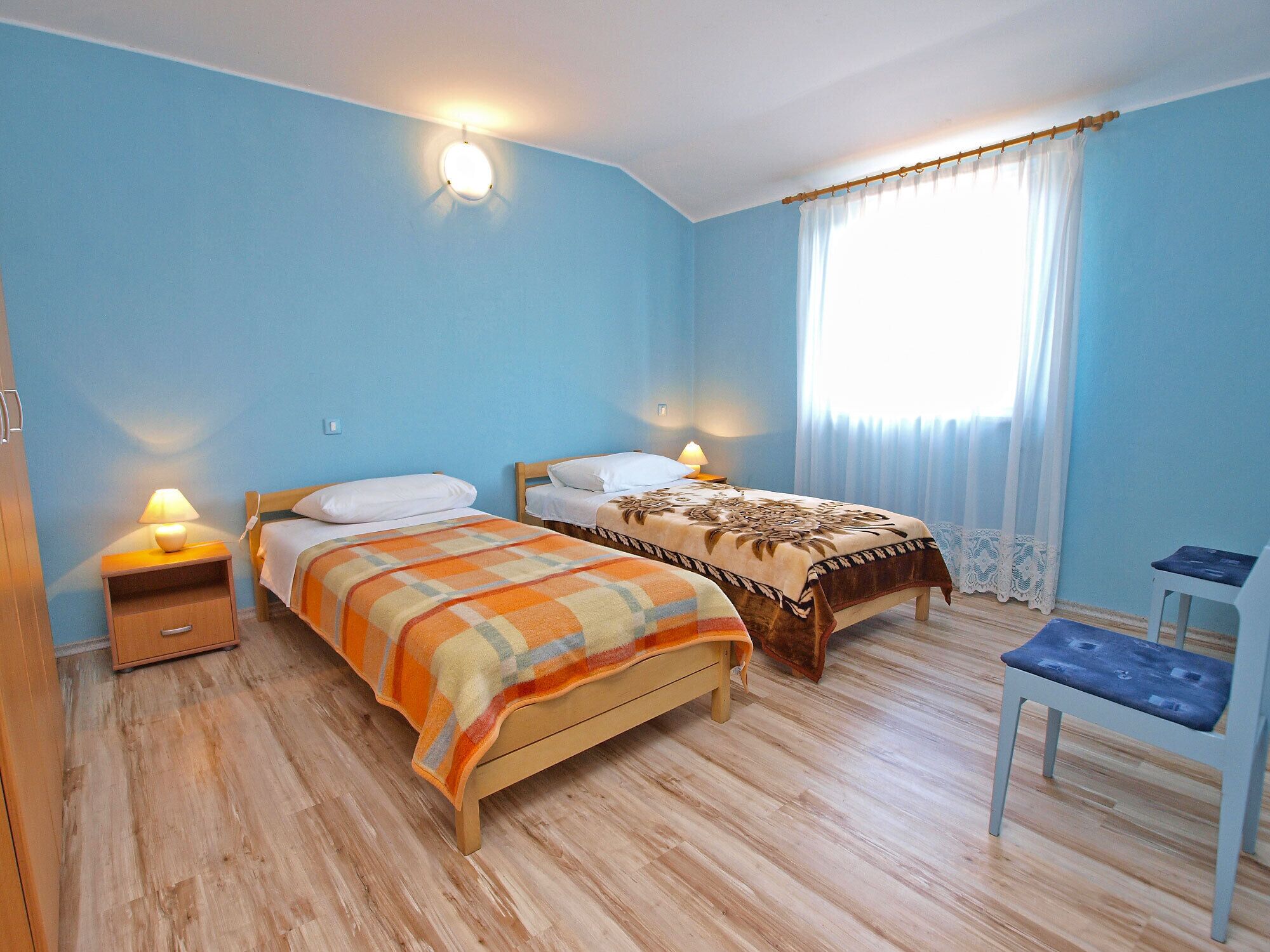 Un dormitorio con dos camas, una silla y una mesita de noche con lámparas.