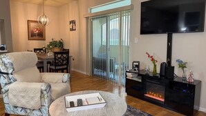 A living room with a sofa, a coffee table, a fireplace, a TV, and a balcony with a sliding door.