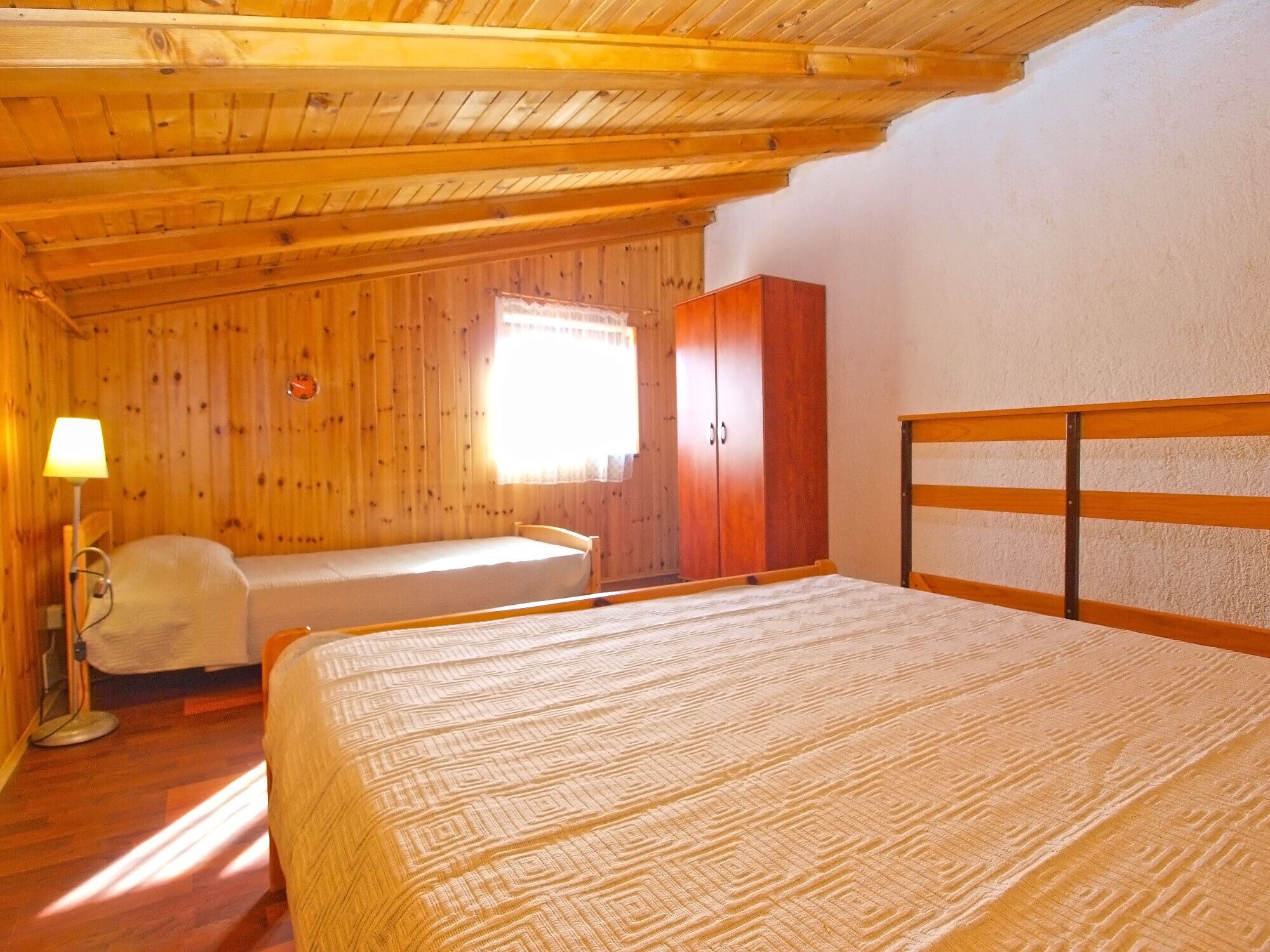 Una habitació de fusta amb un llit, una cadira, un armari i una finestra.