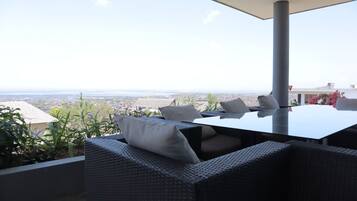 A terrace with wicker furniture, a table, and a view of a cityscape.