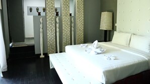 Een hotelkamer met een groot bed, een nachtkastje, een lamp en een wand met decoratieve panelen.