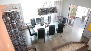 Een moderne eetruimte met een glazen tafel en zwarte stoelen, een bijzondere hanglamp, en uitzicht op de omgeving.
