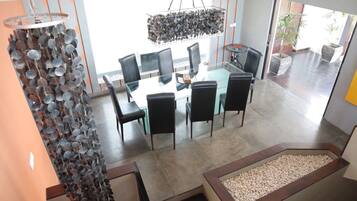 A modern dining area with a glass table and black chairs, a unique hanging light fixture, and a view of the outdoors.