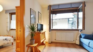 Un accogliente soggiorno con un letto, una televisione, una pianta in vaso e una finestra con tende.