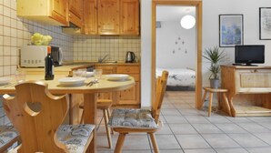 Una cucina compatta con mobili in legno, un tavolo da pranzo con sedie, una televisione e una piccola pianta.