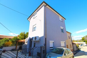 Ein zweistöckiges Gebäude mit flachem Dach, ein Auto davor und eine Treppe, die zum Eingang führt.