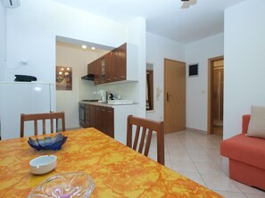 A compact kitchen with wooden cabinets, a dining table with chairs, a red sofa, and a bathroom visible through an open door.