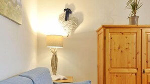 Una habitación con un sofá azul, un armario de madera, una lámpara de pared y una planta pequeña.
