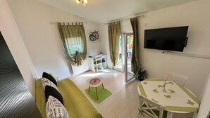 Un espacio habitable compacto con un sofá, una mesa de comedor, un televisor montado en la pared y un patio con puertas de vidrio corredizas.