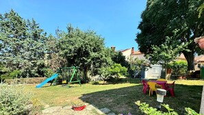 Un patio trasero con un columpio, un tobogán, una mesa con sillas y un parterre de flores.