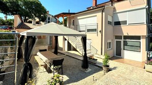 Un edificio residencial con un porche cubierto, mobiliario exterior y una escalera que lleva a un nivel superior.