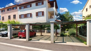 A multi-story residential building with a covered parking area, a red car parked inside, and a sign indicating 'PARTIMANI APARTMENTS'. - Apartment 1293/12300 (Istria - Fažana), 200m from the beach (Fažana)