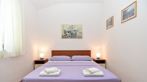 A neatly made bed with two pillows and two folded towels, a wooden headboard, two bedside tables with lamps, and a wall-mounted painting. - Apartment 1293/12300 (Istria - Fažana), 200m from the beach (Fažana)