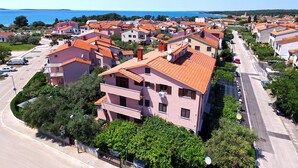 A coastal residential area with terracotta-roofed buildings, a clear blue sky, and a view of the sea. - Apartment 1293/12300 (Istria - Fažana), 200m from the beach (Fažana)