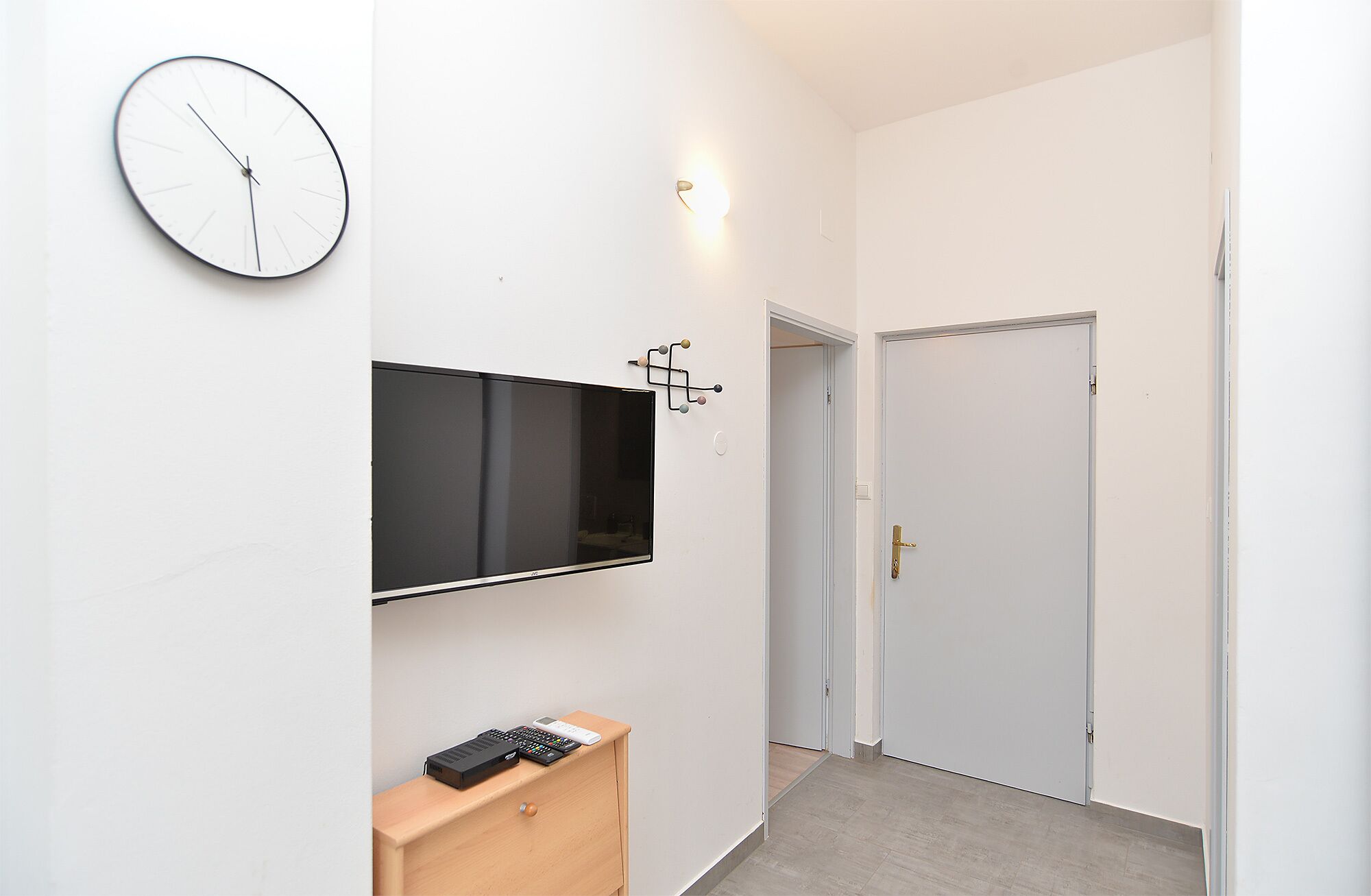 Een hal met een hangend horloge, een flatscreen televisie en een wandlamp.
