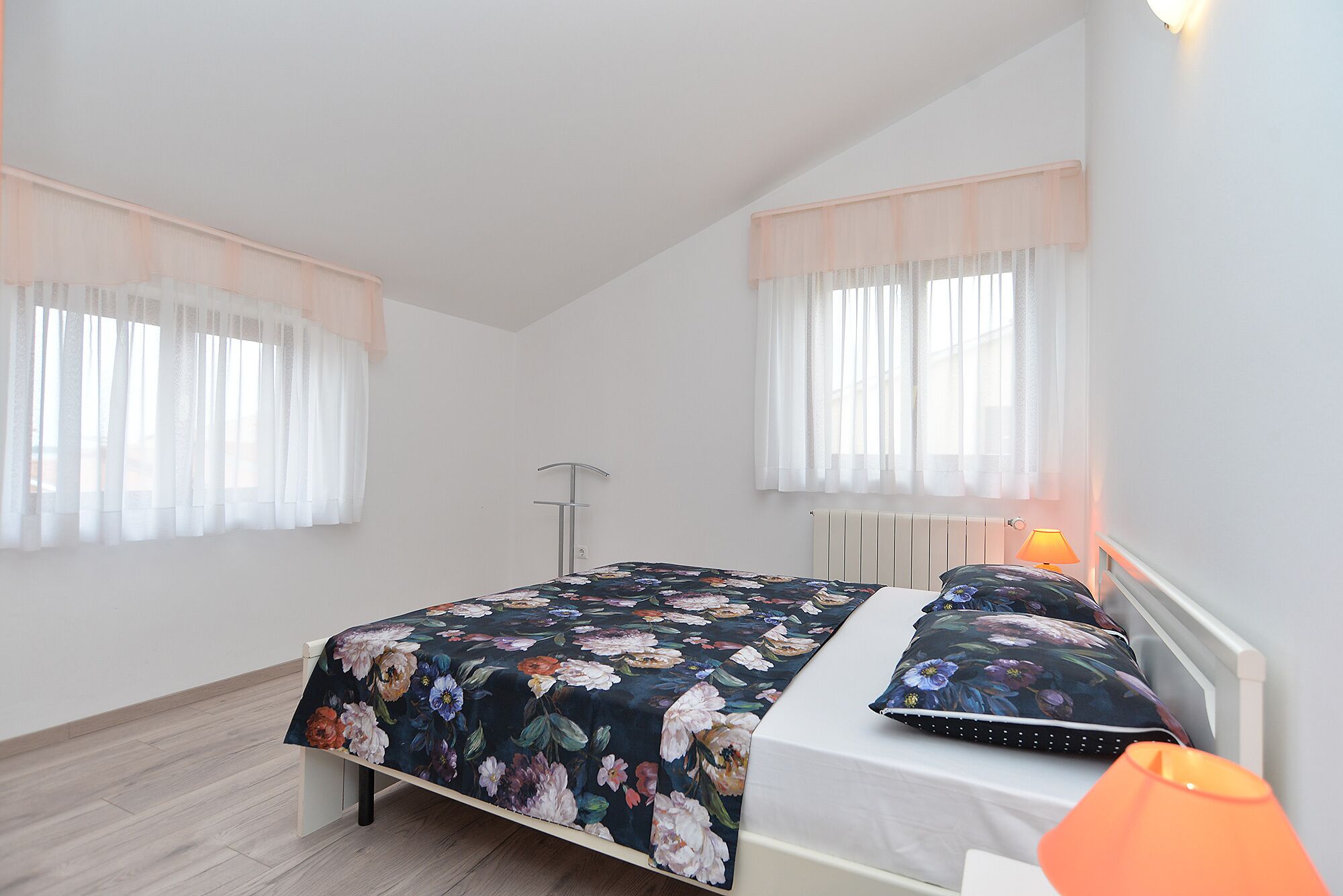 Una camera da letto con due letti, ognuno con lenzuola a motivi floreali, un comodino con una lampada e un termosifone.