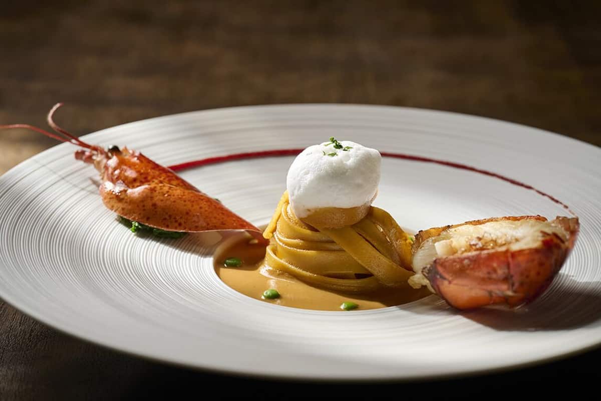A plate with a lobster tail, a mound of what appears to be mashed potatoes, and a stack of pancakes or pancakes with a dollop of cream on top.
