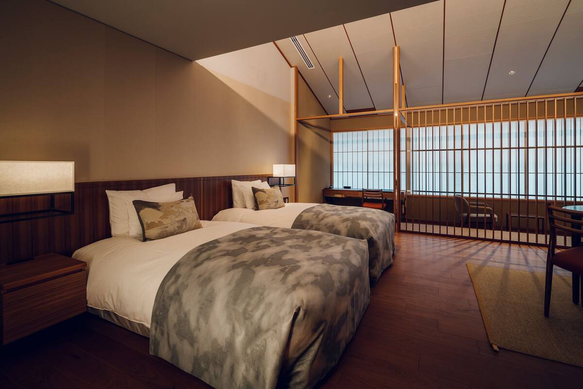 A modern hotel room with two beds, a desk, and a large window.