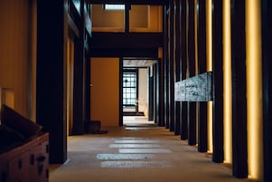 A corridor with wooden pillars, a tiled floor, and a view into another room.