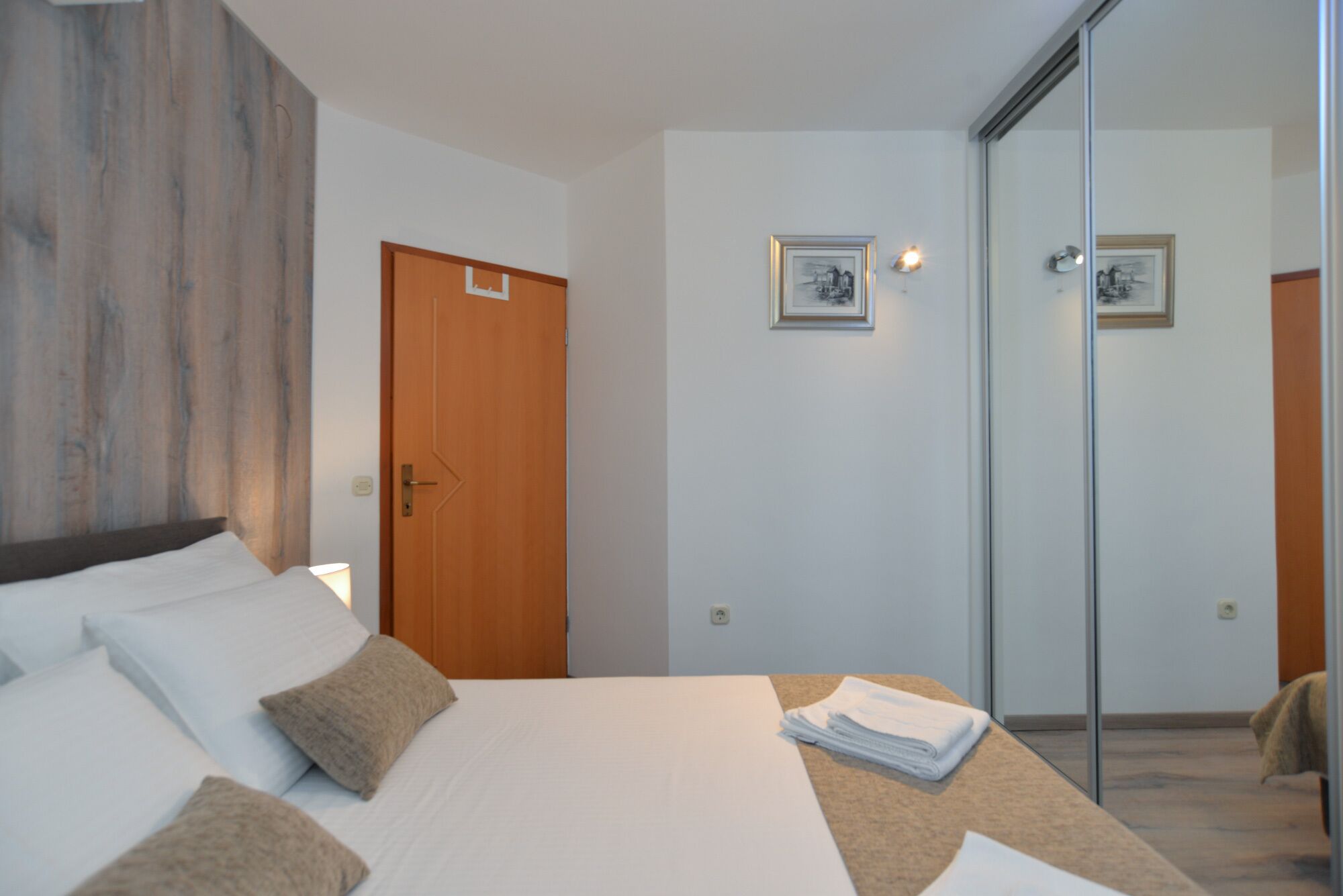 Una camera d'albergo con un letto, una porta in legno, un quadro appeso al muro e una parete divisoria in vetro.