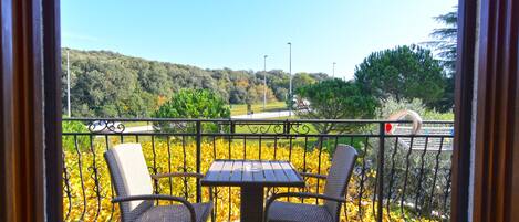 Un balcon avec deux fauteuils en osier et une petite table, offrant une vue panoramique sur une zone boisée et une route.