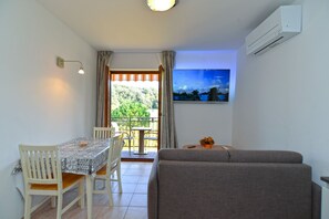 Cozy living space with a dining area and seating area, featuring a table, chairs, sofa, and a view of the lush landscape.