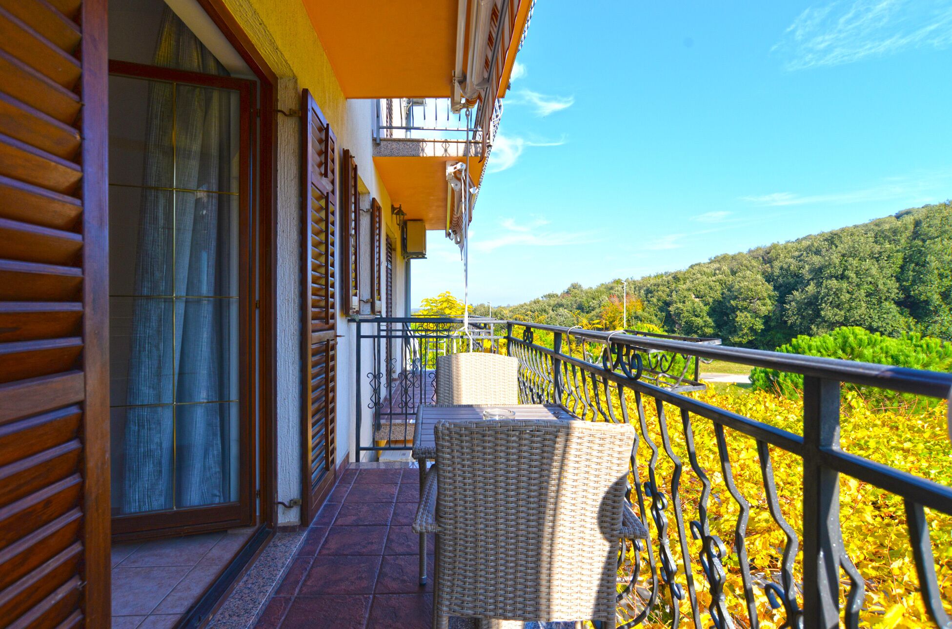 A balcony with wicker furniture, a tiled floor, and a view of a forested hillside.