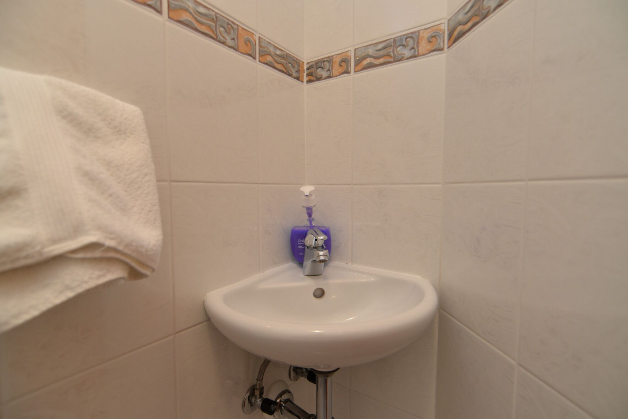 A bathroom with a white sink, a soap dispenser, and a towel hanging on the wall.