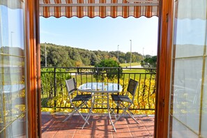 Un balcon avec une table et des chaises, une vue sur un paysage verdoyant et une rambarde en métal.