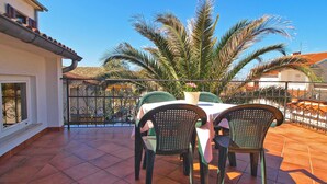Un patio con una mesa y sillas, una planta en maceta y vista a una casa con techo de tejas.
