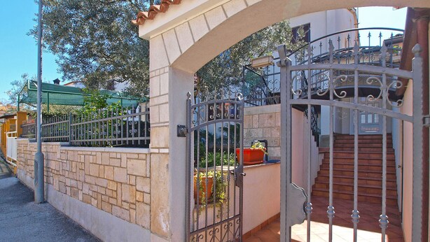 Una entrada protegida con un muro de piedra, una verja metálica y una escalera que lleva a un edificio.