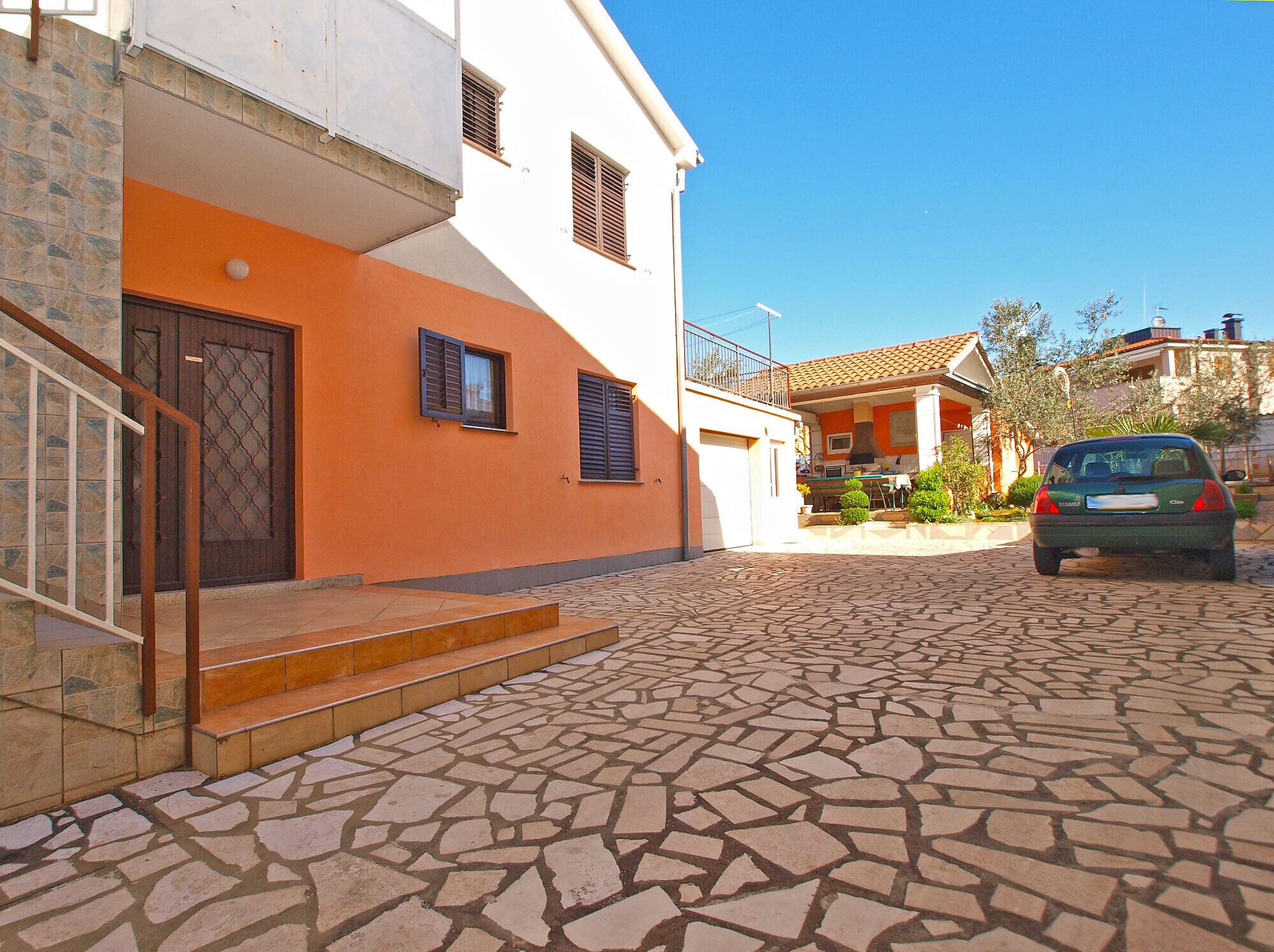 Un edificio de dos pisos con un patio empedrado y un automóvil estacionado.