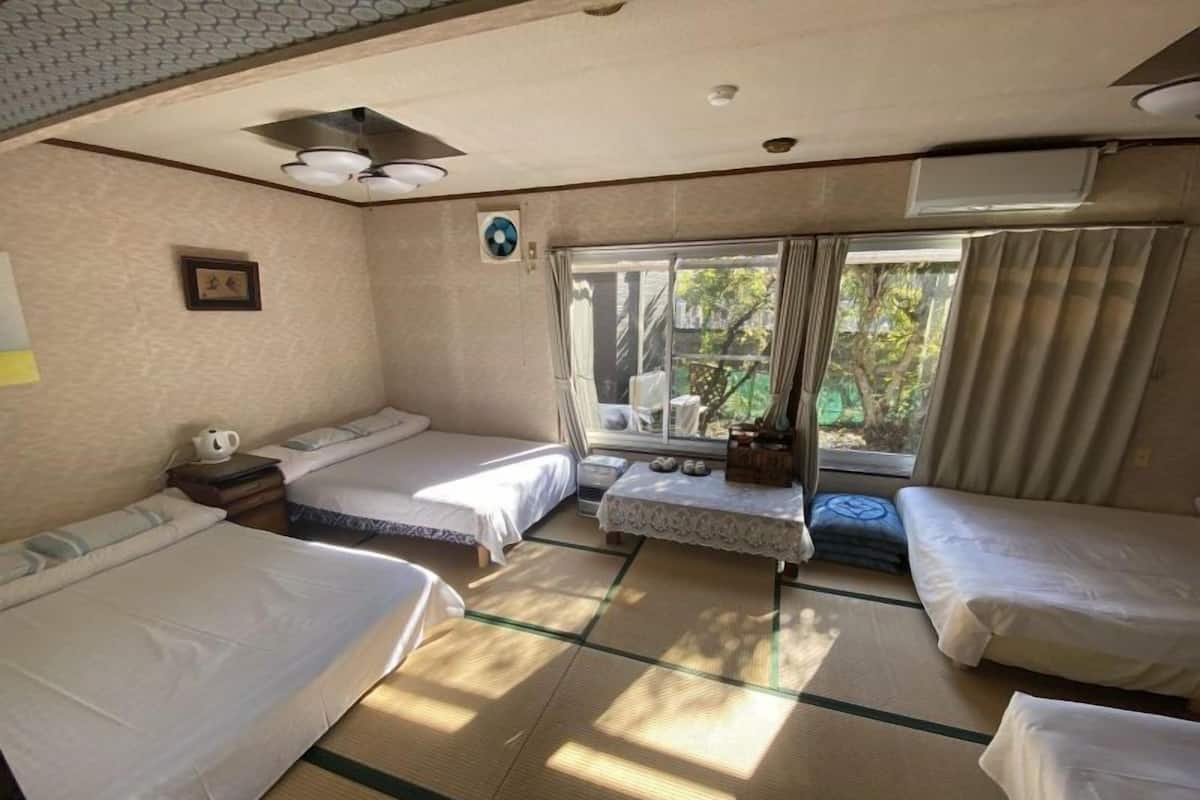 Ein Zimmer mit zwei Betten, einem kleinen Tisch und einem Fenster mit Vorhängen.