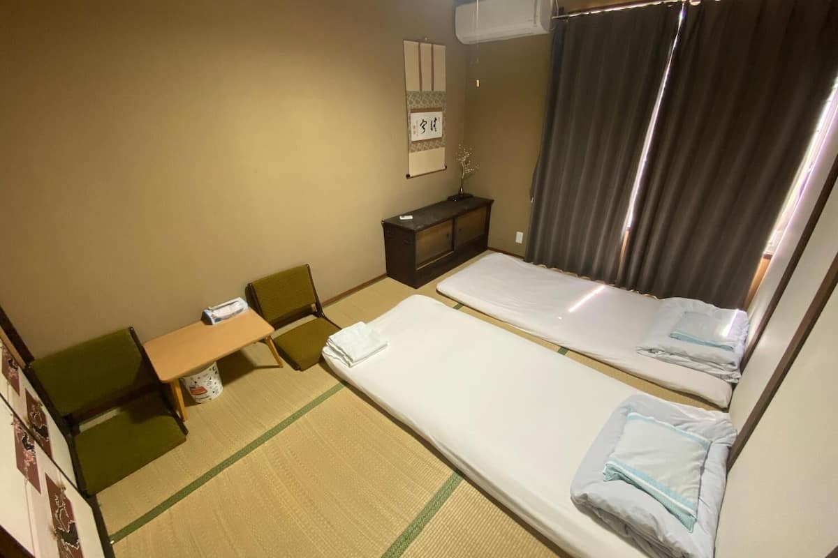 Ein Hotelzimmer mit zwei Betten, einem kleinen Schreibtisch, einem Sessel, einem Fernseher und einem Vorhang.