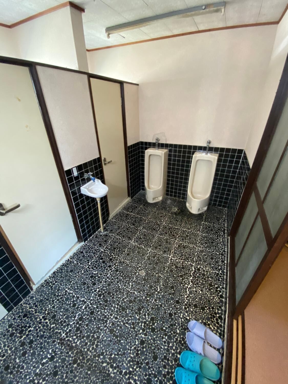Un bagno maschile con due orinatoi, un lavandino e un pavimento piastrellato.