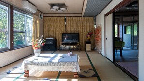 Une pièce de style japonais traditionnel, avec un sol recouvert de tatamis, une petite table recouverte d’une nappe, un téléviseur et un vase rempli de fleurs.