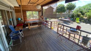 Une terrasse en bois avec une table et des chaises, une fenêtre et une vue sur un jardin.