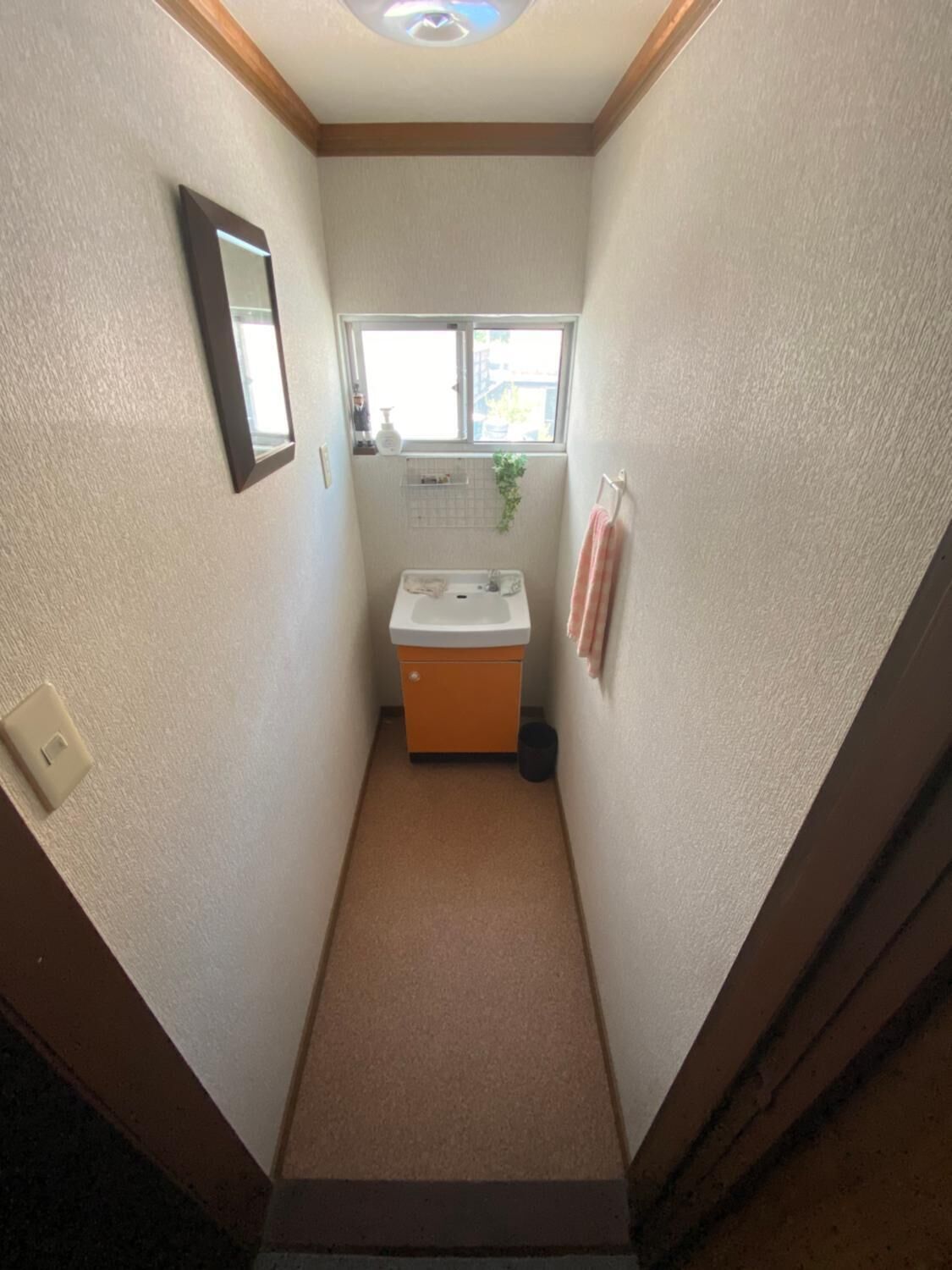 Ein schmales Badezimmer mit Waschbecken, Spiegel, Fenster und Handtuchhalter.