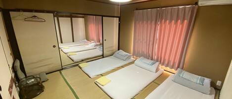 Quarto de hotel com três camas de solteiro, um espelho grande, luminária pendente e porta de correr.