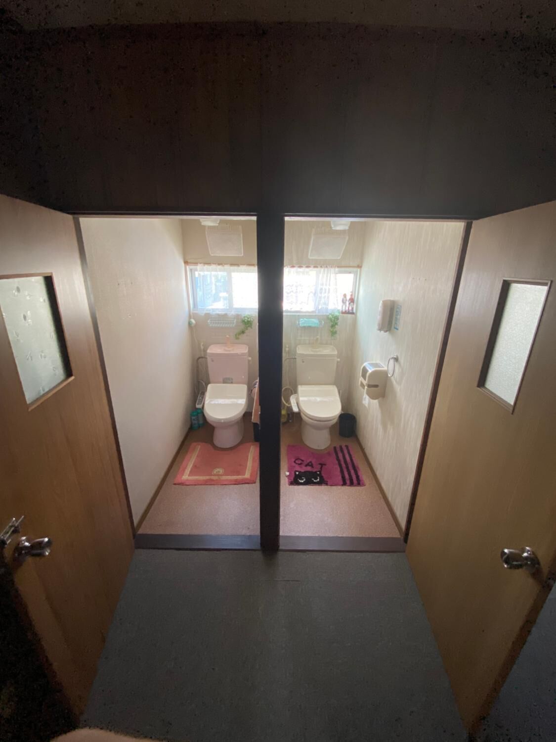 Un baño pequeño con dos inodoros, un lavamanos y una ventana.