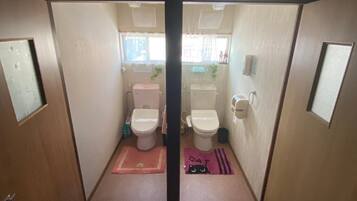 A compact bathroom with two toilets, a sink, and a window.