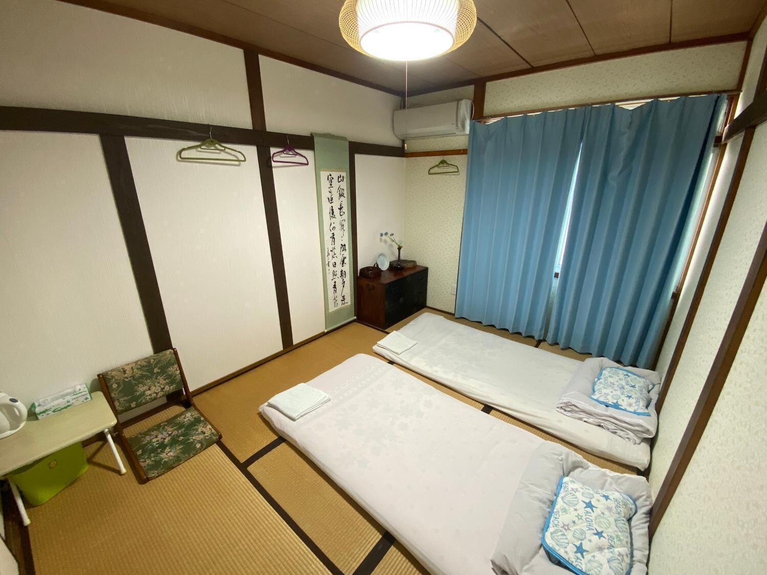 A traditional Japanese room with tatami flooring, two beds, a small desk, and a hanging toilet paper dispenser.