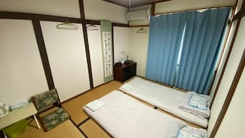 A traditional Japanese room with tatami flooring, two beds, a small desk, and a hanging toilet paper dispenser.