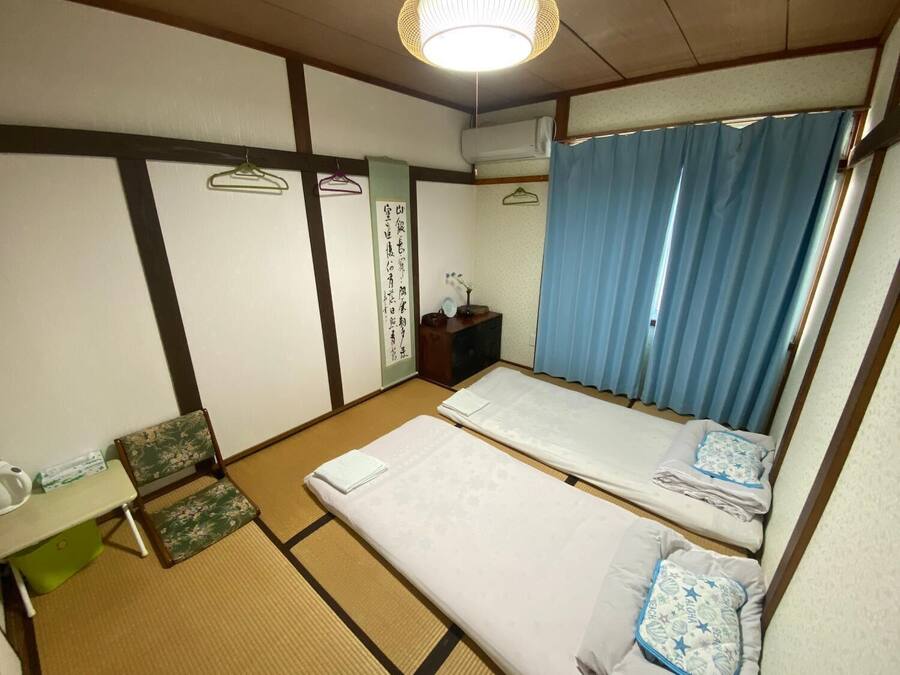 A traditional Japanese room with tatami flooring, two beds, a small desk, and a hanging toilet paper dispenser.