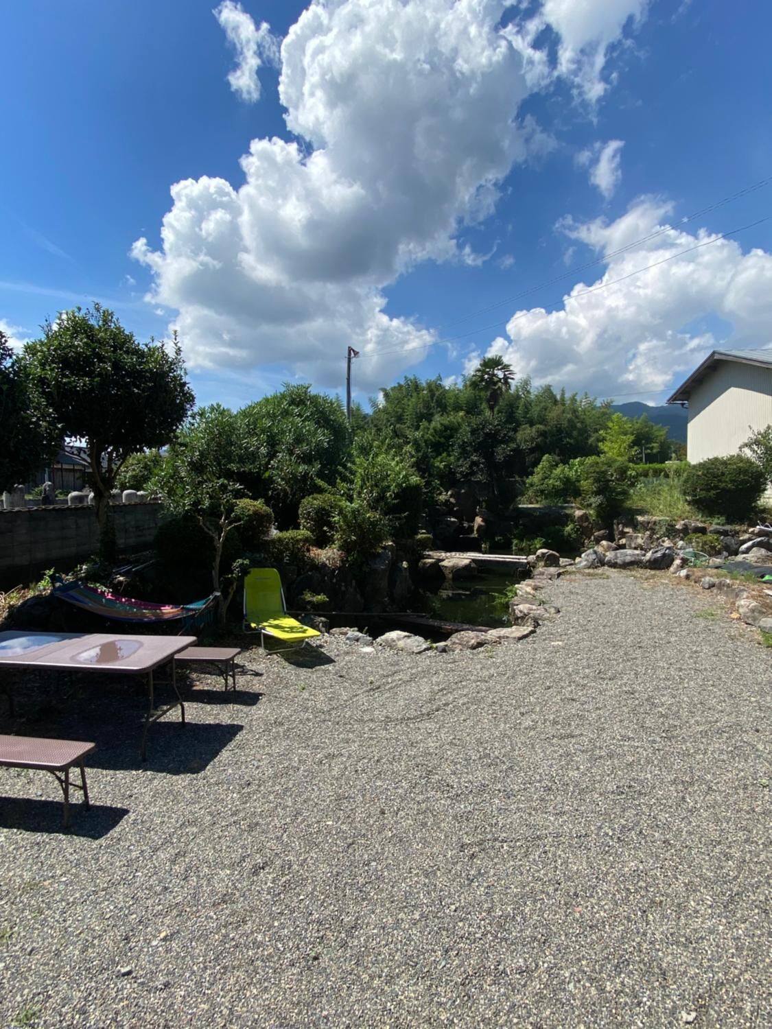 Une terrasse en gravier avec des meubles d’extérieur, un petit étang et de la verdure tout autour.