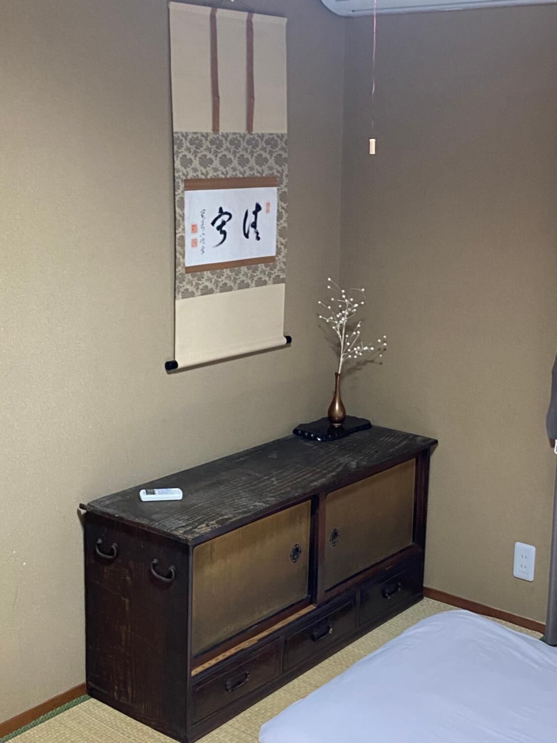 A bedroom with a bed, a dresser, a wall-mounted shelf with a decorative item, and a wall with a hanging sign.