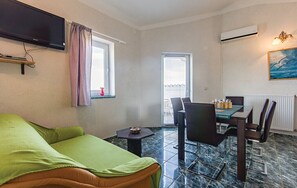 A living room with a green sofa, a dining table with chairs, a TV mounted on the wall, and a window with curtains. - Apartment 1328/12573 (Istria - Fažana), 500m from the beach (Fažana)